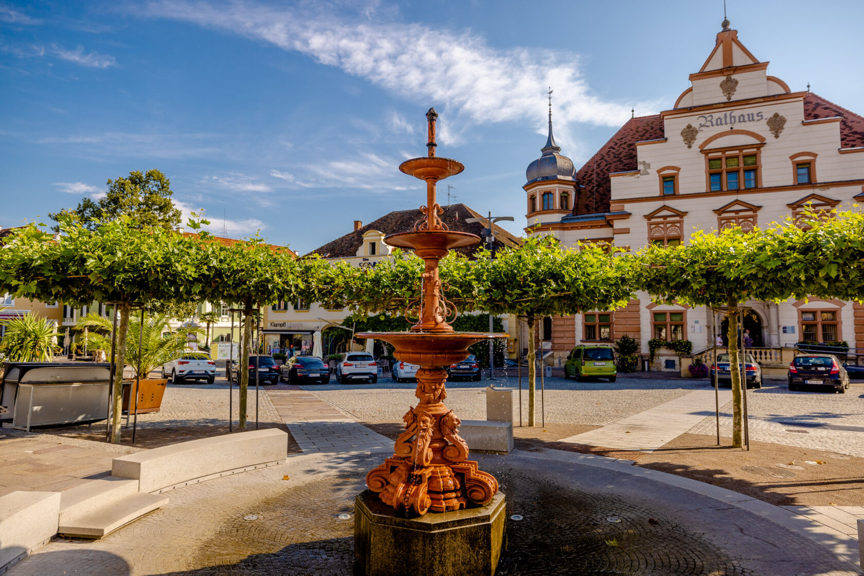 Brunnen und Rathaus in der kleinen historischen Stadt Hartberg bei strahlendem Sonnenschein.